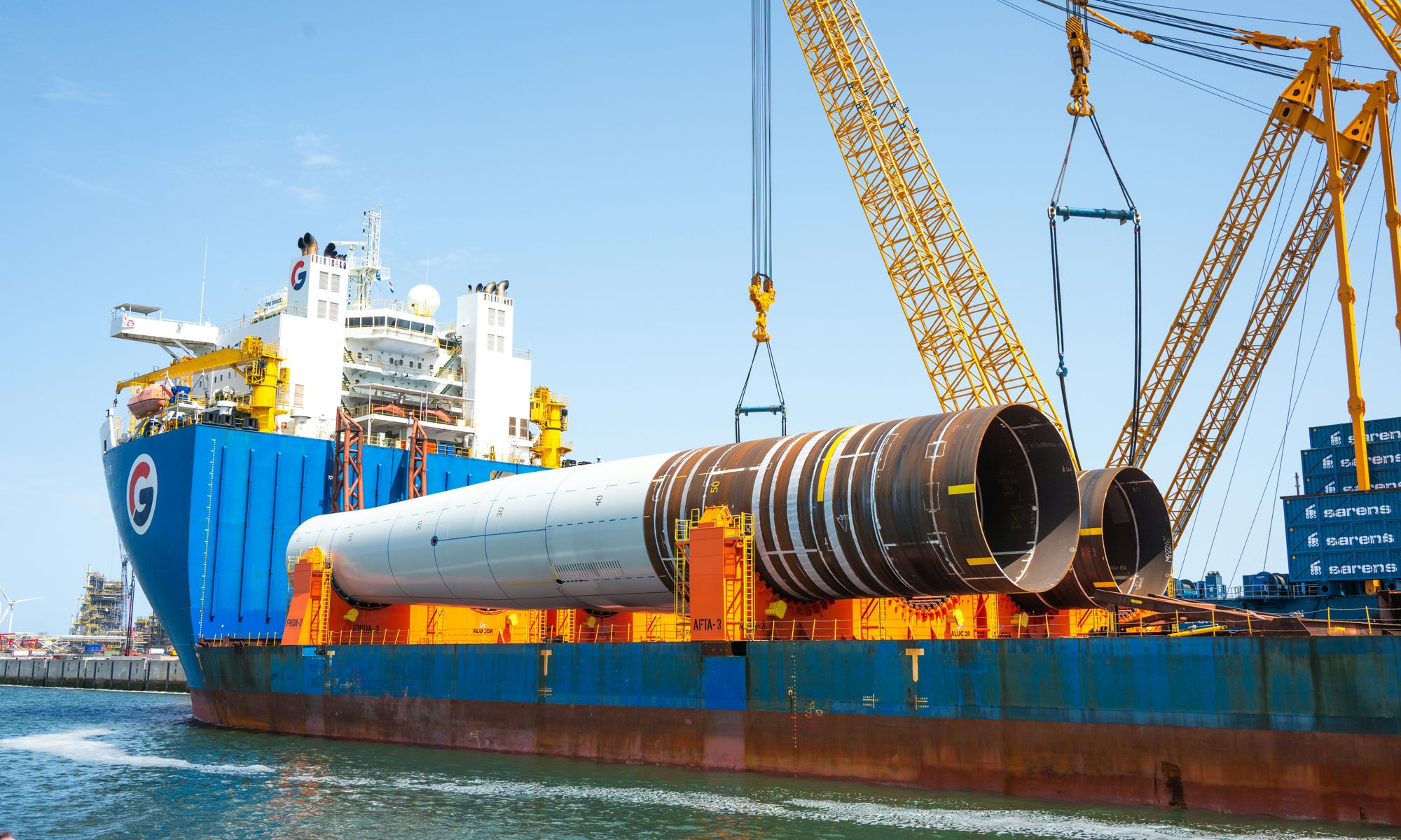 A heavy-lift ship loading steel pipe sections with cranes